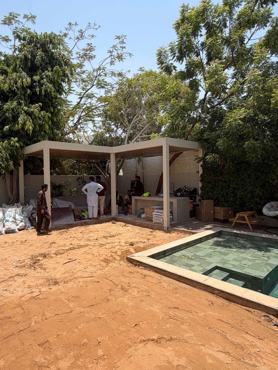 Same courtyard mid-construction, bare sand and unfinished pergola.