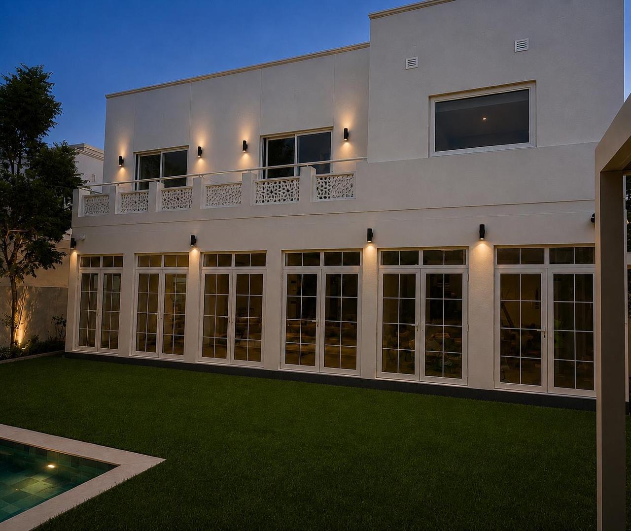 Villa rear facade at dusk with lit windows and pool.